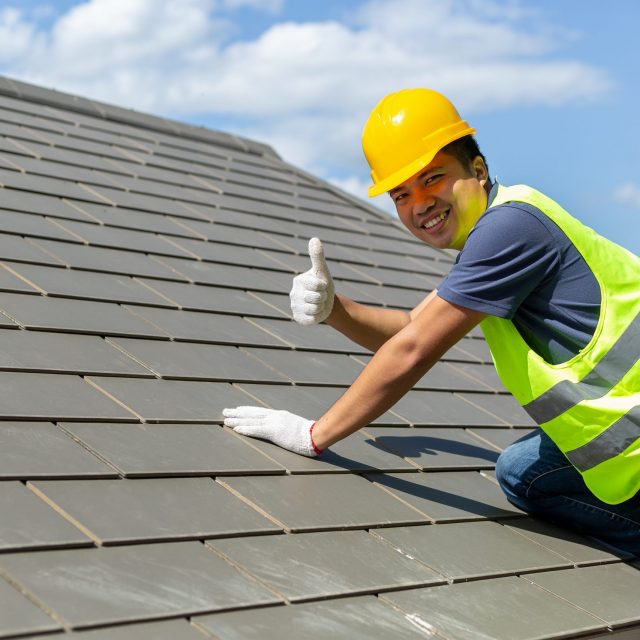 Asian tile roofing workers, smiling at the camera, lifted their thumbs to indicate the stability of the roof.